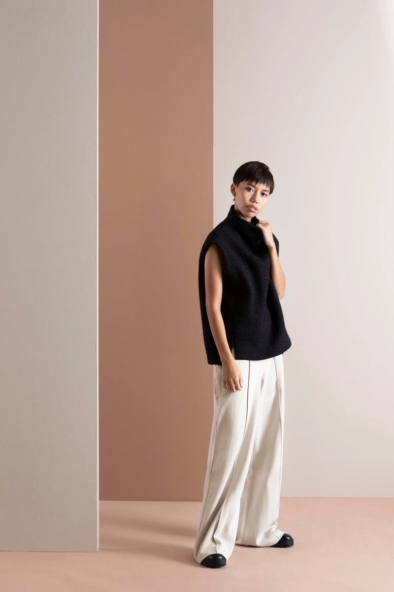 Model wearing a black sleeveless high-neck vest with white wide-leg trousers