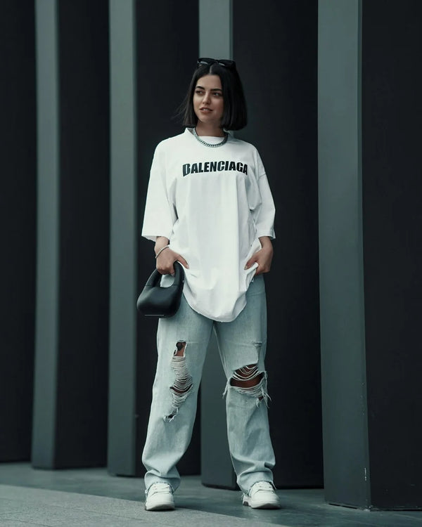 Model wearing a white oversized long-sleeve top with black chest lettering and distressed jeans