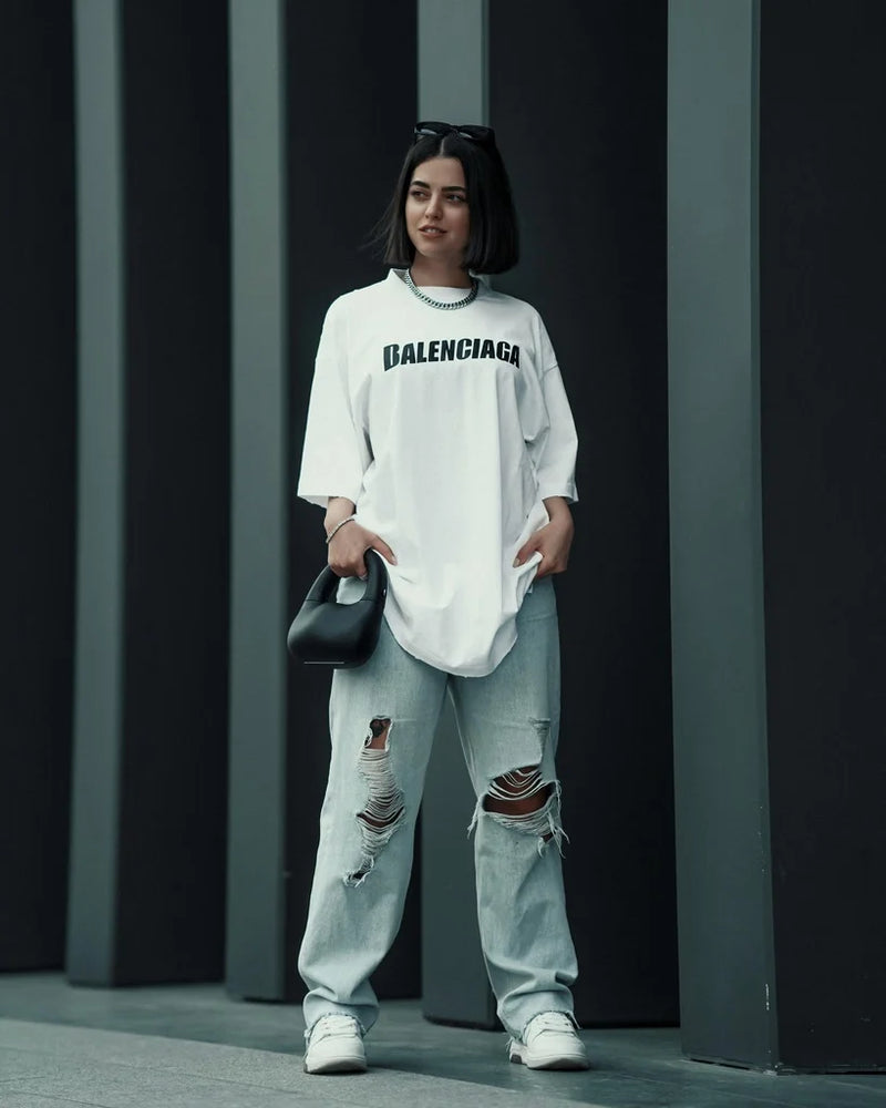 Model wearing a white oversized long-sleeve top with black chest lettering and distressed jeans