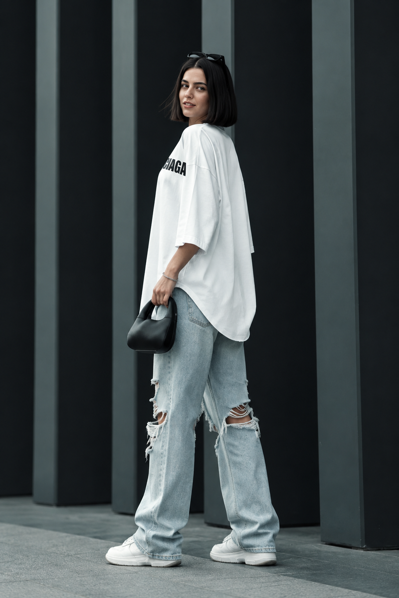 Rear three-quarter view of a model wearing a white oversized logo long-sleeve top