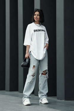 Three-quarter view of a model wearing a white oversized logo long-sleeve top