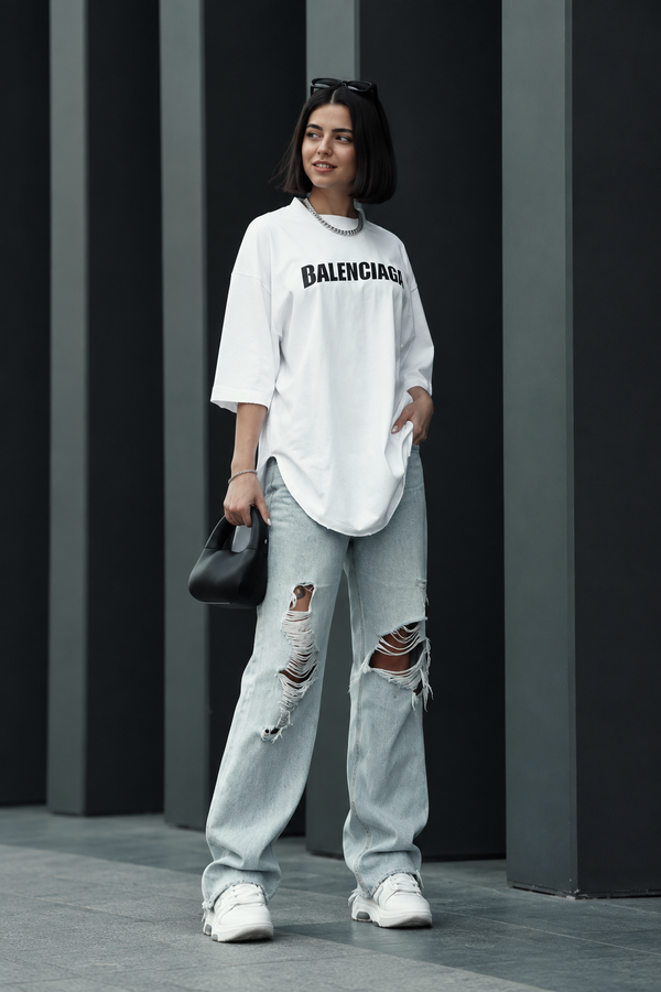 Three-quarter view of a model wearing a white oversized logo long-sleeve top